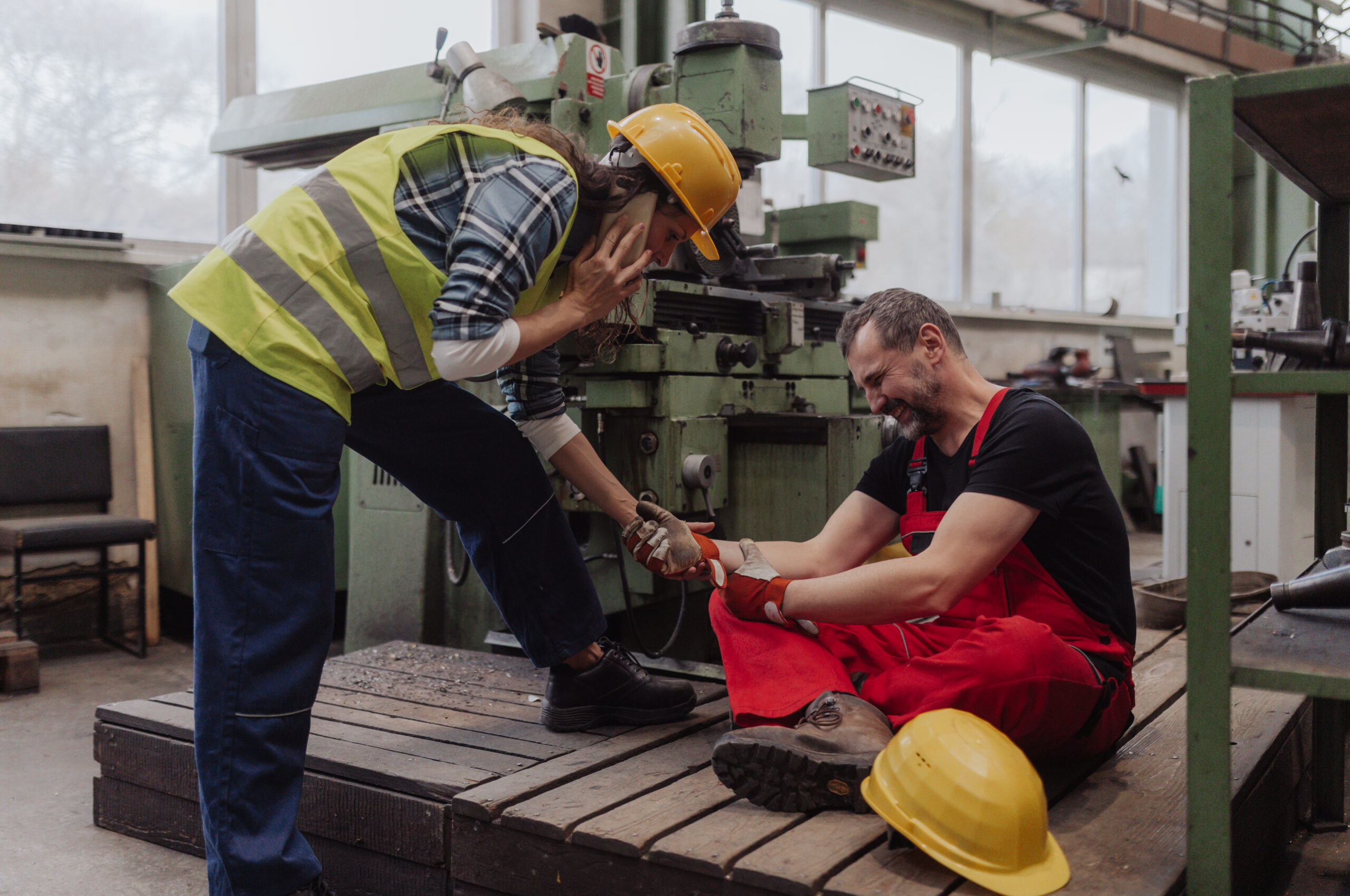 A woman is helping her colleague after accident in factory. First aid support on workplace concept.